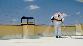 a-man-in-a-white-coverall-spray-painting-a-roof