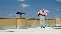 a-man-in-a-white-coverall-spray-painting-a-roof