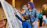 participants at the 2025 The Big Draw. Child draws on cavas, woman with purple hair watches