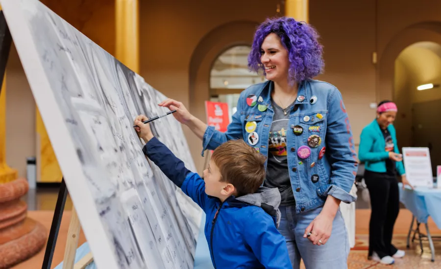 participants at the 2025 The Big Draw. Child draws on cavas, woman with purple hair watches
