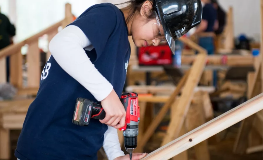 young woman wearing hardhat drills into a piece of wood