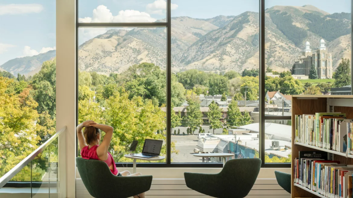 Logan City Library interior. Window outlooks mountain range. woman sits in chair looking out