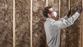 a man wearing a mask installs insulation into a wall system