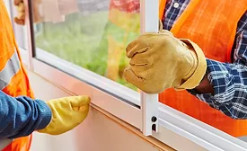 two men install a window wearing work gloves and orange safety vests