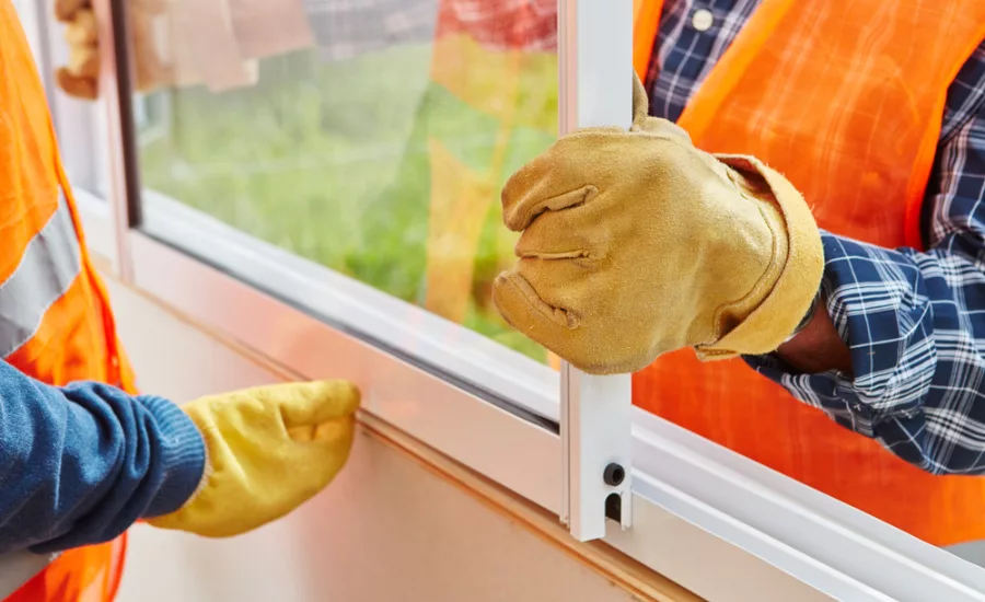 two men install a window wearing work gloves and orange safety vests