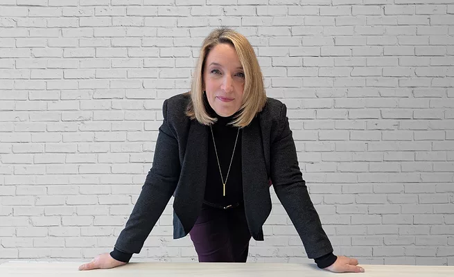Jaime Masler Beach.png Jaime Masler Beach headshot. Jamie stands over a table and leans into the camera